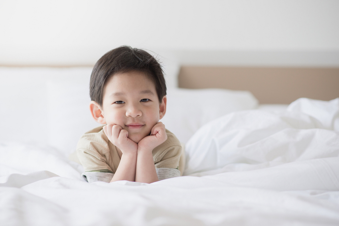 How to transition toddler from crib to bed. Cute Asian toddler lying on white bed.