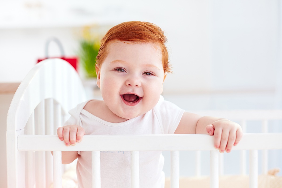 cute happy infant baby standing in a cot at home won't sleep